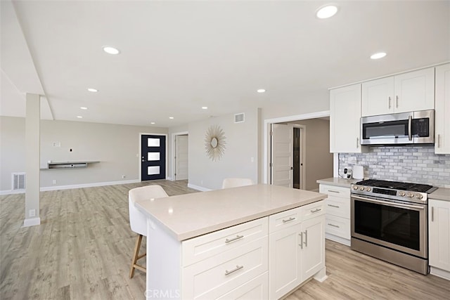 kitchen featuring appliances with stainless steel finishes, white cabinets, a center island, light hardwood / wood-style floors, and tasteful backsplash