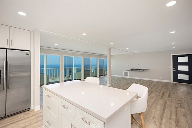 kitchen featuring fridge, white cabinetry, a center island, a water view, and light hardwood / wood-style flooring