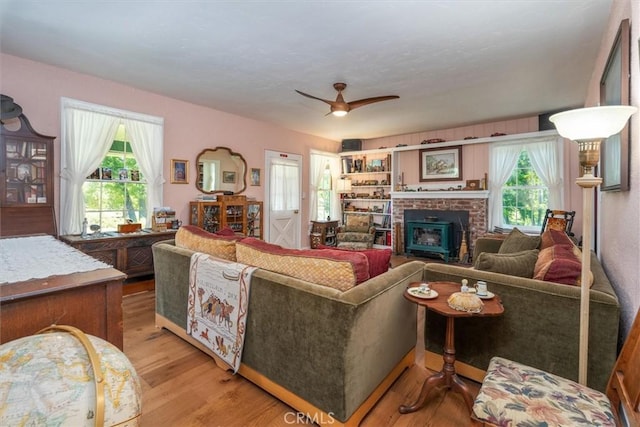 living room with light hardwood / wood-style floors, a wood stove, a wealth of natural light, and ceiling fan