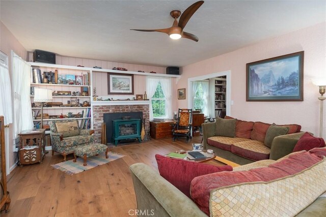 living room featuring a wood stove, ceiling fan, and wood-type flooring