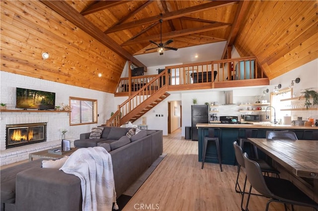 living area with a fireplace, wood ceiling, a ceiling fan, light wood finished floors, and beamed ceiling