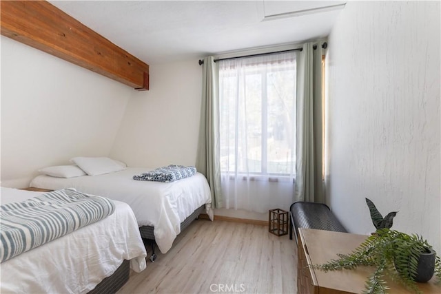 bedroom featuring light wood-style floors, multiple windows, and beamed ceiling