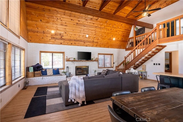 living room with high vaulted ceiling, a brick fireplace, wooden ceiling, and light wood finished floors