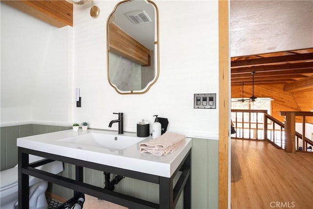 bathroom with a wainscoted wall, wooden walls, visible vents, and beamed ceiling