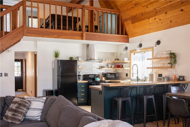 kitchen with open shelves, black appliances, wall chimney range hood, a peninsula, and a kitchen breakfast bar