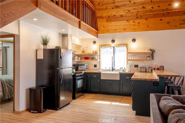 kitchen featuring light wood finished floors, wooden counters, black appliances, and open shelves