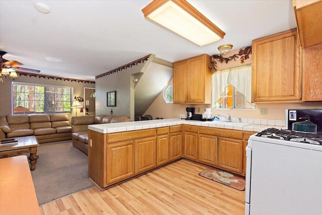 kitchen with ceiling fan, kitchen peninsula, light hardwood / wood-style flooring, white gas range oven, and tile countertops