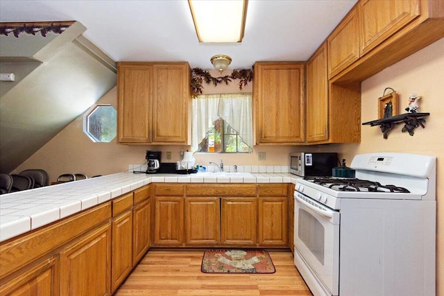 kitchen featuring tile countertops, white gas range oven, light hardwood / wood-style flooring, and sink