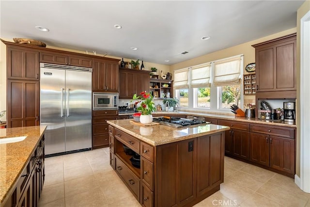 kitchen with built in appliances, light stone counters, a center island, and light tile patterned floors