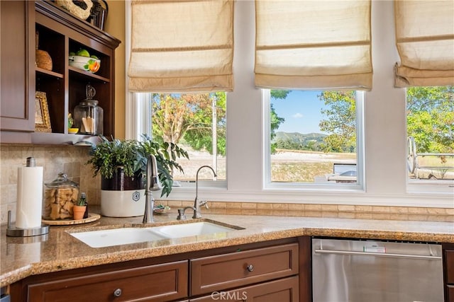 kitchen featuring backsplash, light stone counters, sink, and stainless steel dishwasher