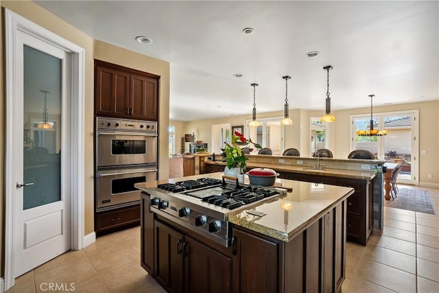 kitchen with light stone countertops, appliances with stainless steel finishes, dark brown cabinetry, a chandelier, and a kitchen island