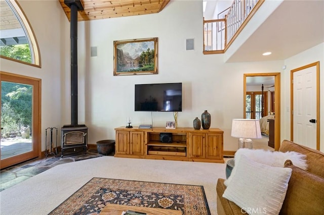 carpeted living room featuring wooden ceiling, a wood stove, a wealth of natural light, and a towering ceiling