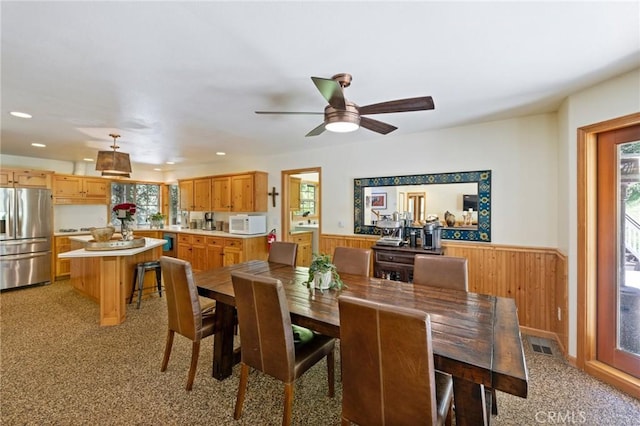 dining room featuring ceiling fan, light colored carpet, and wood walls