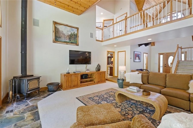 living room featuring a towering ceiling, a wood stove, and wooden ceiling