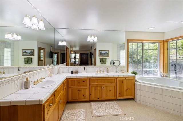 bathroom with backsplash, tiled tub, vanity, and an inviting chandelier