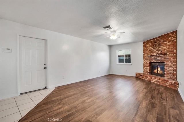 unfurnished living room featuring a brick fireplace, a textured ceiling, ceiling fan, and light hardwood / wood-style floors