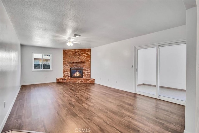 unfurnished living room with a brick fireplace, a textured ceiling, ceiling fan, and hardwood / wood-style flooring