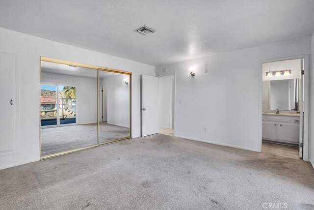 unfurnished bedroom with light colored carpet, a closet, and ensuite bath