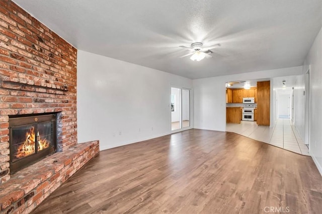 unfurnished living room featuring ceiling fan, light wood-type flooring, and a brick fireplace