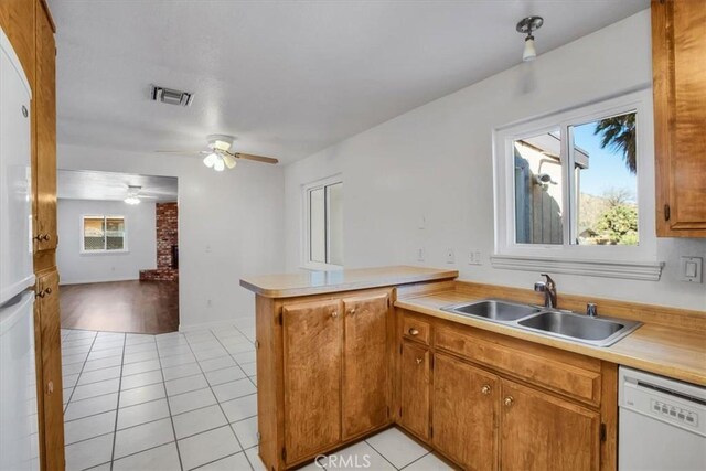 kitchen featuring white appliances, kitchen peninsula, light tile patterned floors, plenty of natural light, and sink