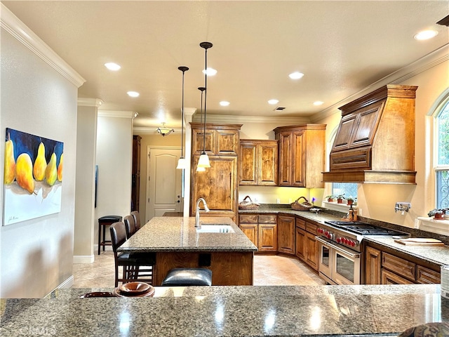 kitchen with ornamental molding, range with two ovens, a kitchen island with sink, decorative light fixtures, and sink