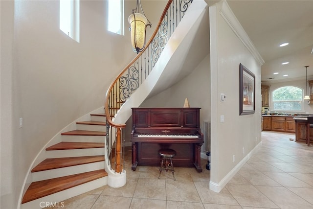 staircase featuring a high ceiling, ornamental molding, and light tile flooring