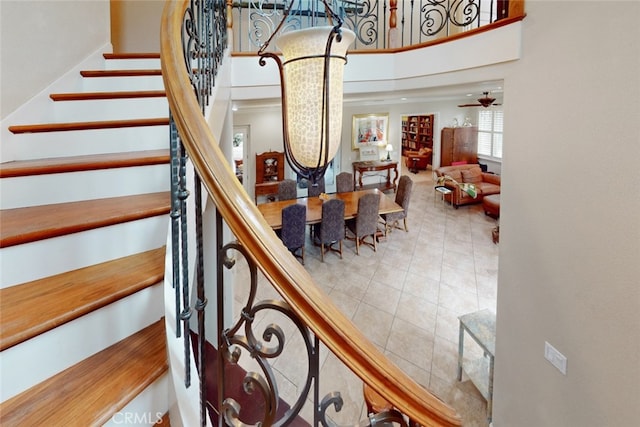 stairway with a towering ceiling, tile flooring, and ceiling fan