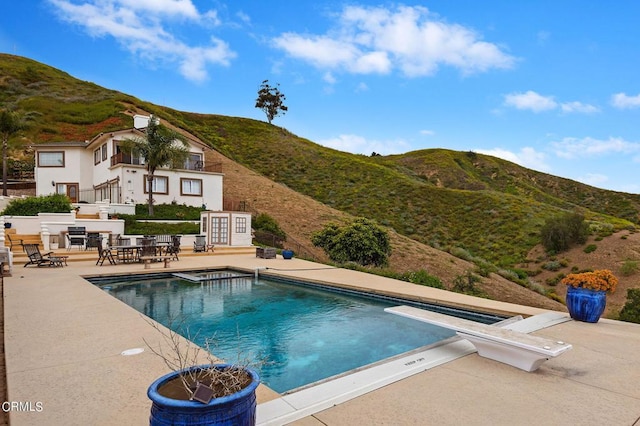 view of swimming pool with a mountain view, a diving board, and a patio