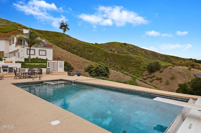 view of swimming pool with a mountain view, a diving board, and a patio