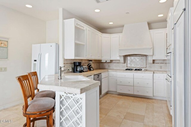 kitchen featuring white appliances, white cabinetry, decorative backsplash, custom exhaust hood, and kitchen peninsula