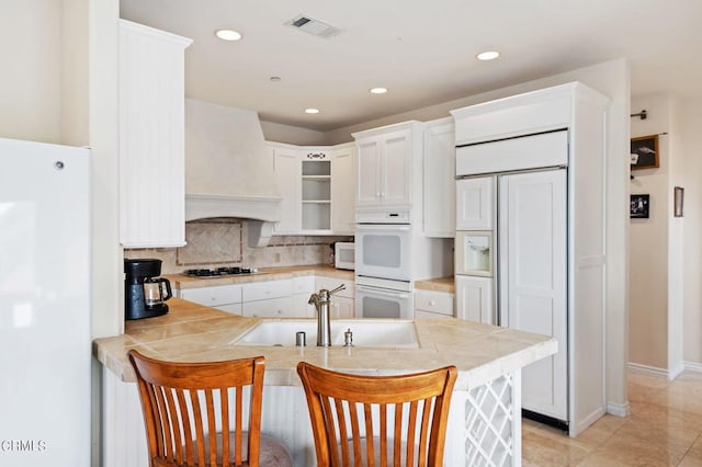 kitchen featuring a breakfast bar, sink, white cabinetry, kitchen peninsula, and white appliances