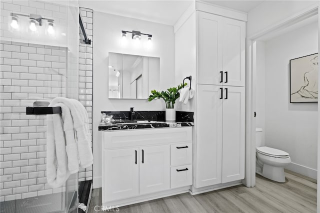 bathroom with tiled shower, vanity, toilet, and hardwood / wood-style floors