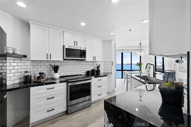 kitchen featuring sink, stainless steel appliances, a water view, white cabinets, and dark stone counters