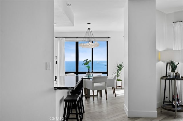 dining space featuring a water view, light wood-type flooring, and an inviting chandelier