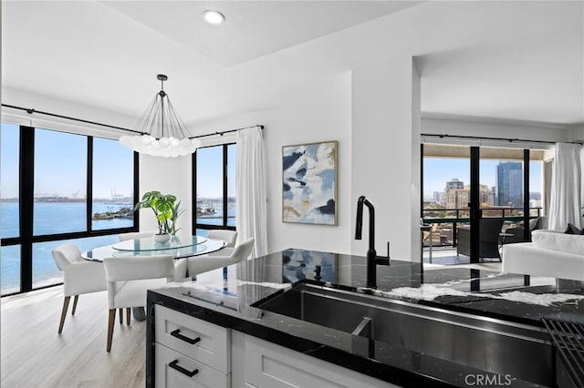 kitchen with a water view, decorative light fixtures, a chandelier, dark stone counters, and white cabinets