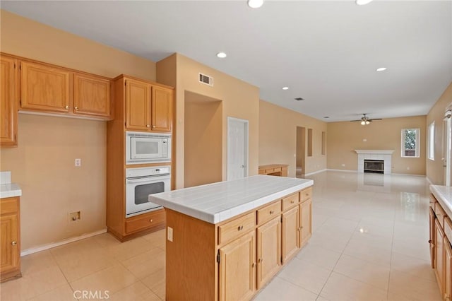 kitchen with white appliances, ceiling fan, a tile fireplace, light tile patterned floors, and tile countertops