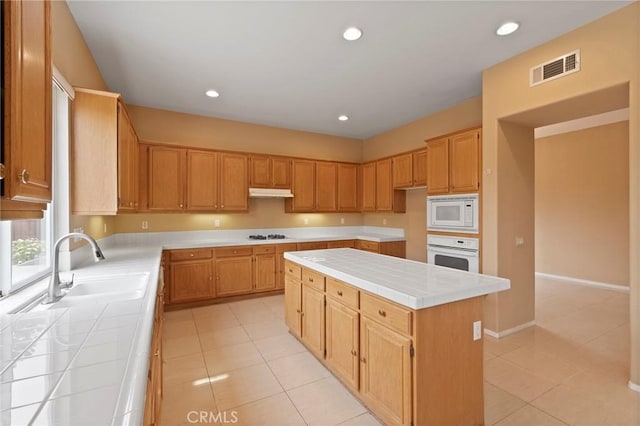 kitchen featuring white appliances, a center island, tile counters, and light tile patterned flooring