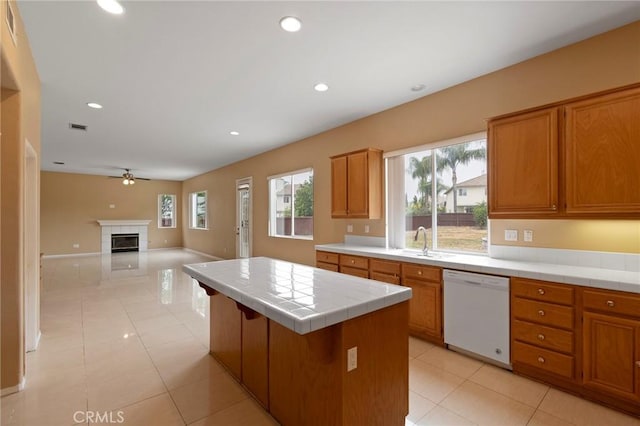 kitchen featuring ceiling fan, a center island, tile countertops, white dishwasher, and a fireplace