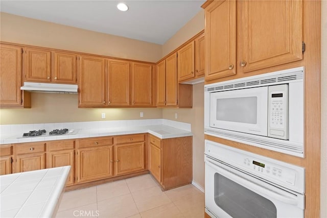 kitchen with light tile patterned floors, white appliances, and tile countertops