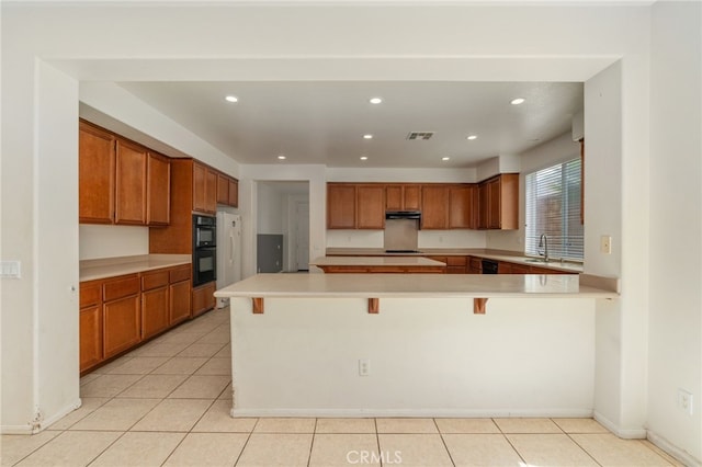 kitchen featuring sink, light tile flooring, black double oven, and a kitchen bar