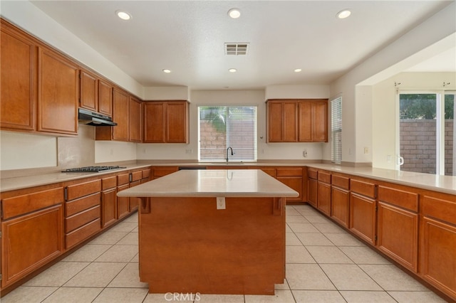 kitchen featuring a kitchen island, stainless steel gas stovetop, a breakfast bar, sink, and light tile floors