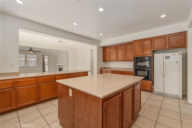 kitchen with white refrigerator, double oven, ceiling fan, a center island, and light tile floors