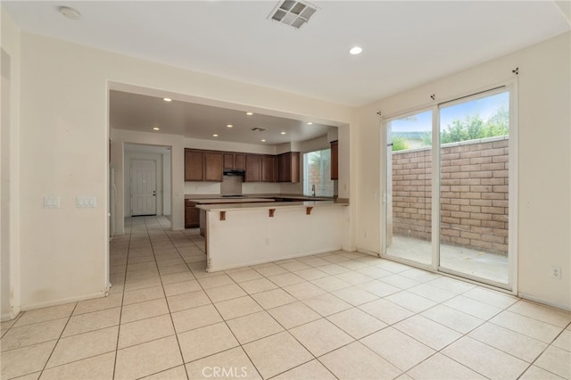 kitchen featuring a kitchen breakfast bar, exhaust hood, kitchen peninsula, and light tile floors