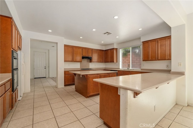 kitchen featuring a kitchen island, a breakfast bar area, kitchen peninsula, gas cooktop, and light tile floors