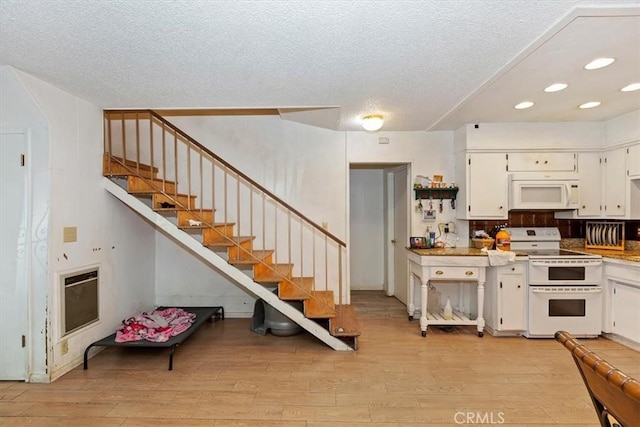 kitchen with a textured ceiling, white appliances, heating unit, light hardwood / wood-style floors, and white cabinetry