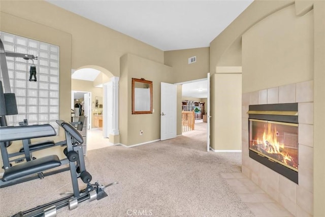 exercise area with lofted ceiling, light carpet, and a tiled fireplace