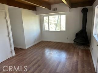 unfurnished bedroom with a wood stove, hardwood / wood-style floors, wood ceiling, and beam ceiling