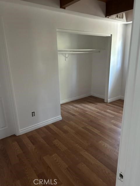 unfurnished bedroom featuring beamed ceiling, dark hardwood / wood-style floors, and a closet