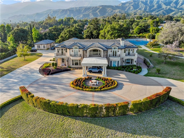 view of front facade featuring a mountain view, a balcony, and a front lawn