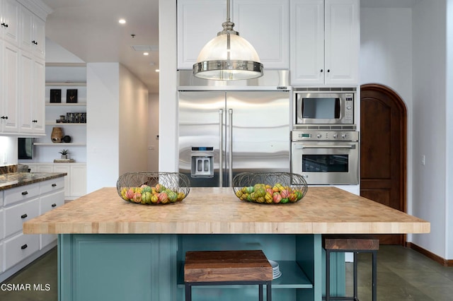 kitchen with built in appliances, a center island, pendant lighting, and white cabinets